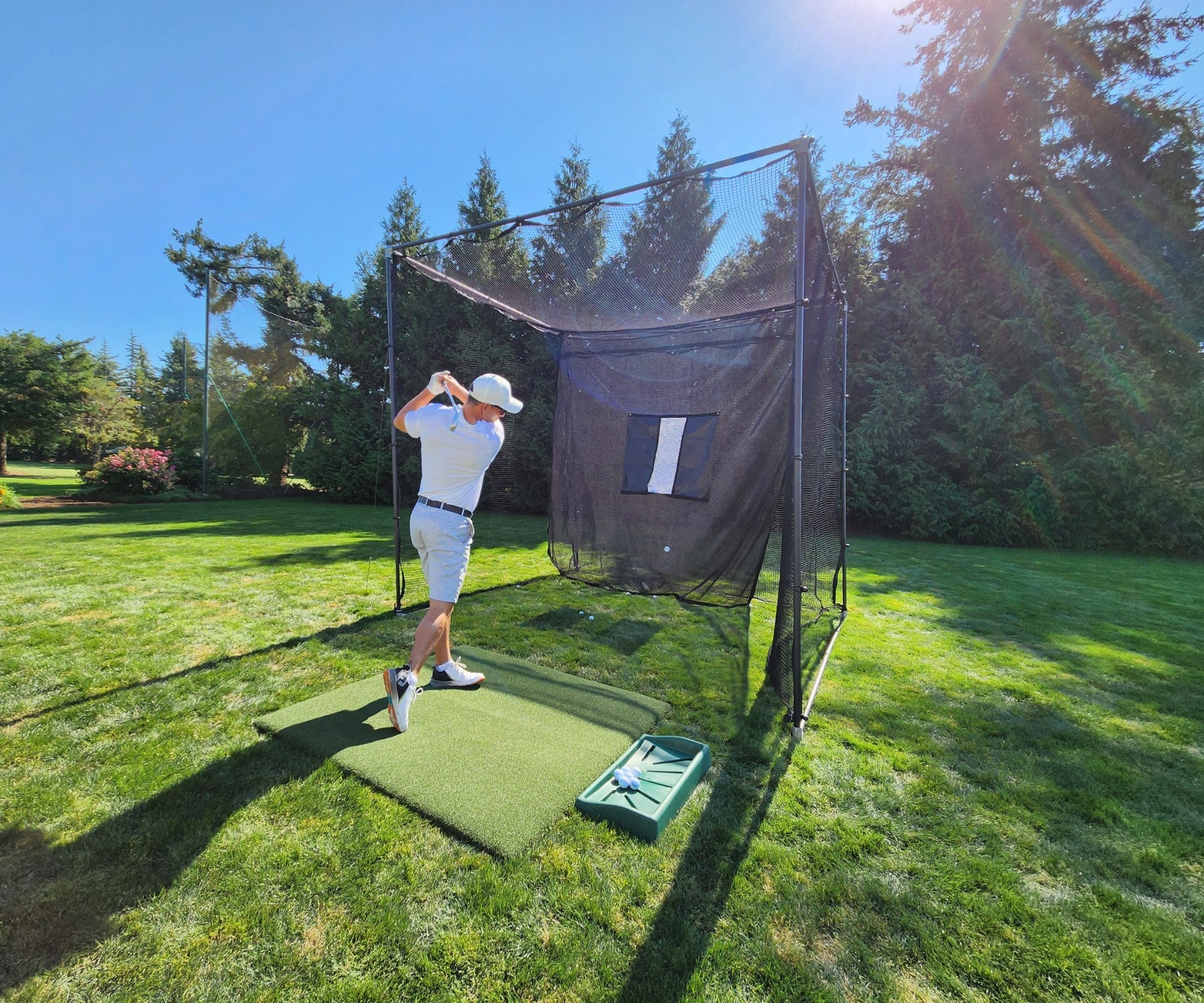 Man hitting golf balls into golf cage netting in backyard 
