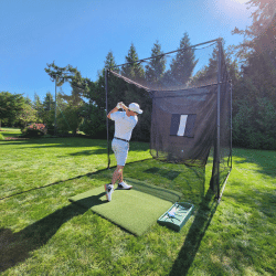 Man hitting golf balls into a golf cage with green grass and trees