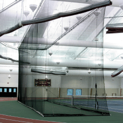 Tall batting cage net inside field house with bright lights above.